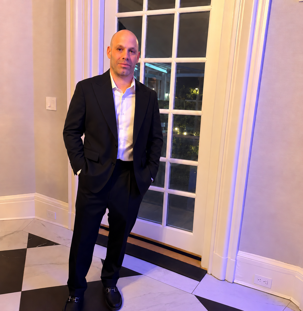 Camilo Valencia, owner of Valencia Consulting, wearing a dark suit and open-collar white shirt